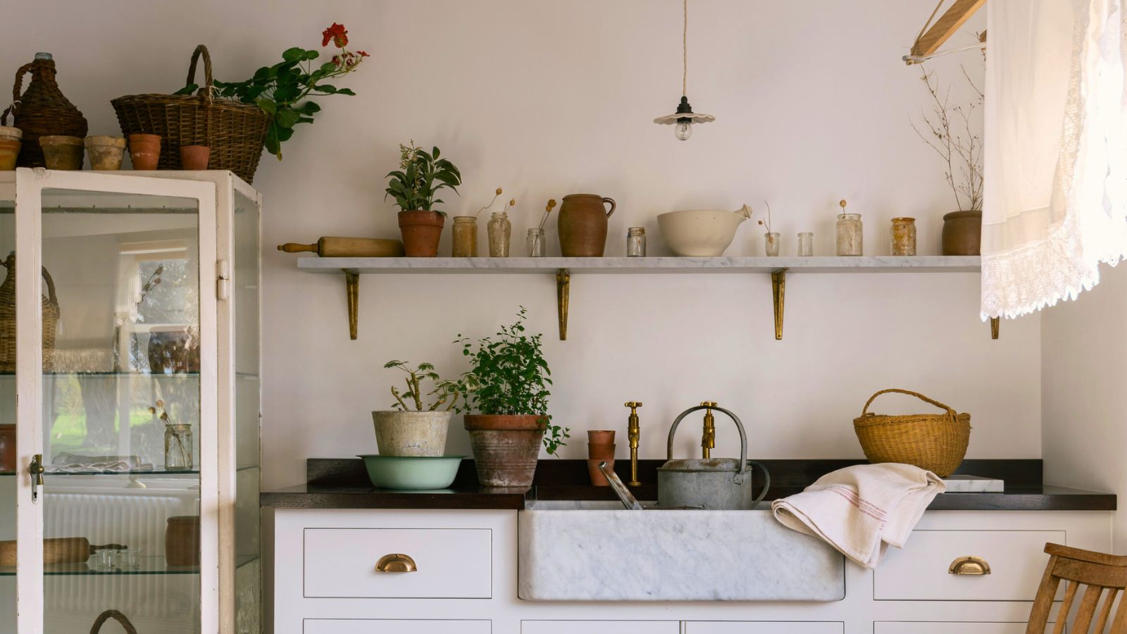 Cottage laundry room with hanging rail, open shelving, butler sink, glass cabinet and mismatched pots in natural materials