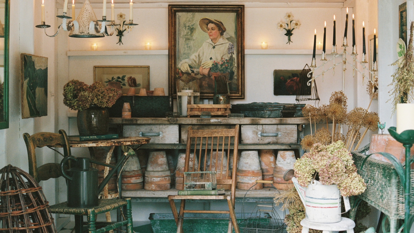 The indoors of a vintage-themed potting shed with pots, antique chairs and paintings