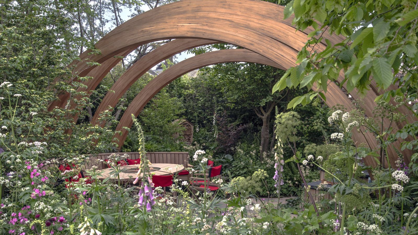 A show garden at Chelsea Flower Show with trees, shrubs, and flowering perennials under a large wooden arch