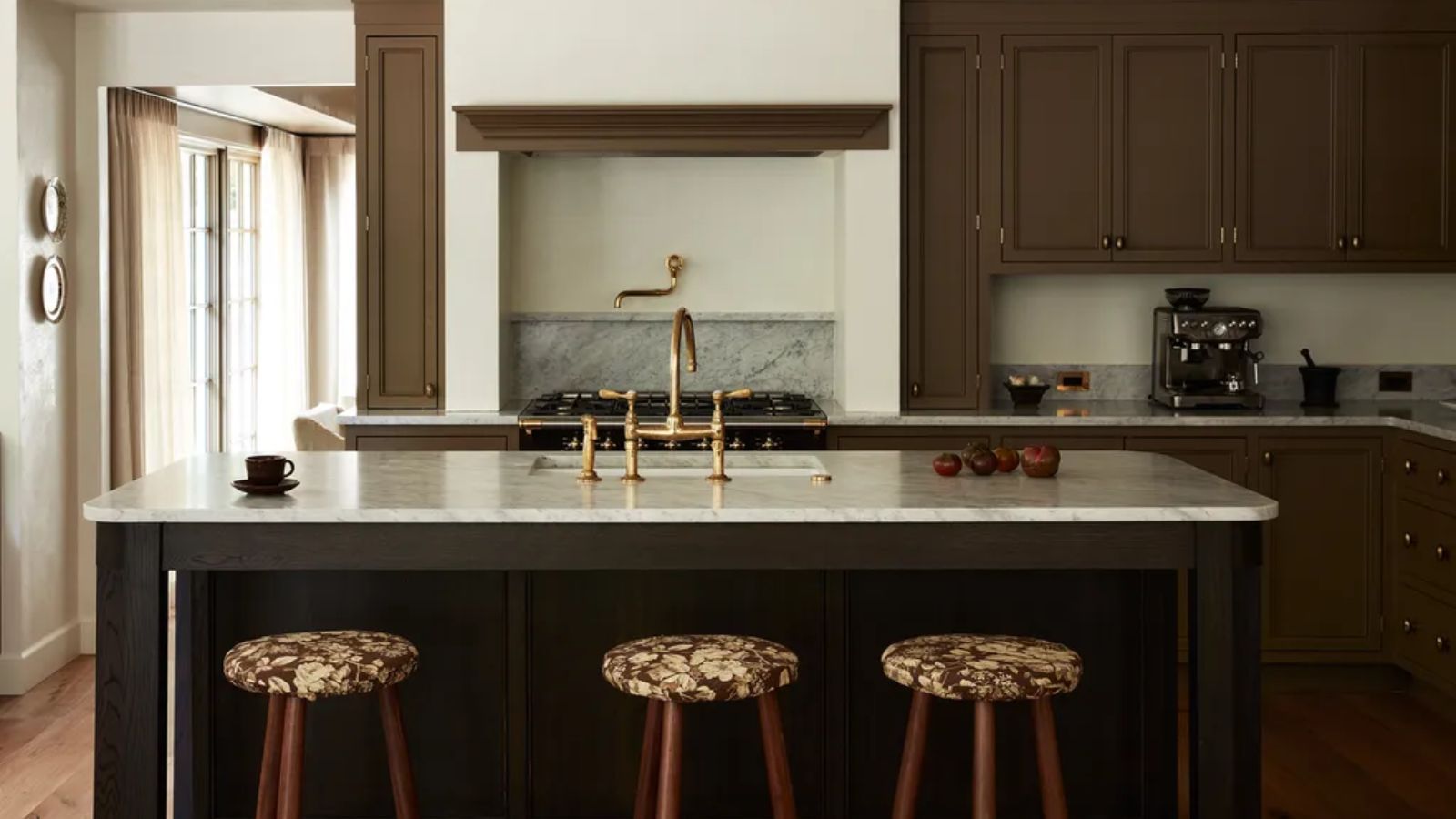 A kitchen with brown painted cabinets and white marble countertops. Gold fixtures