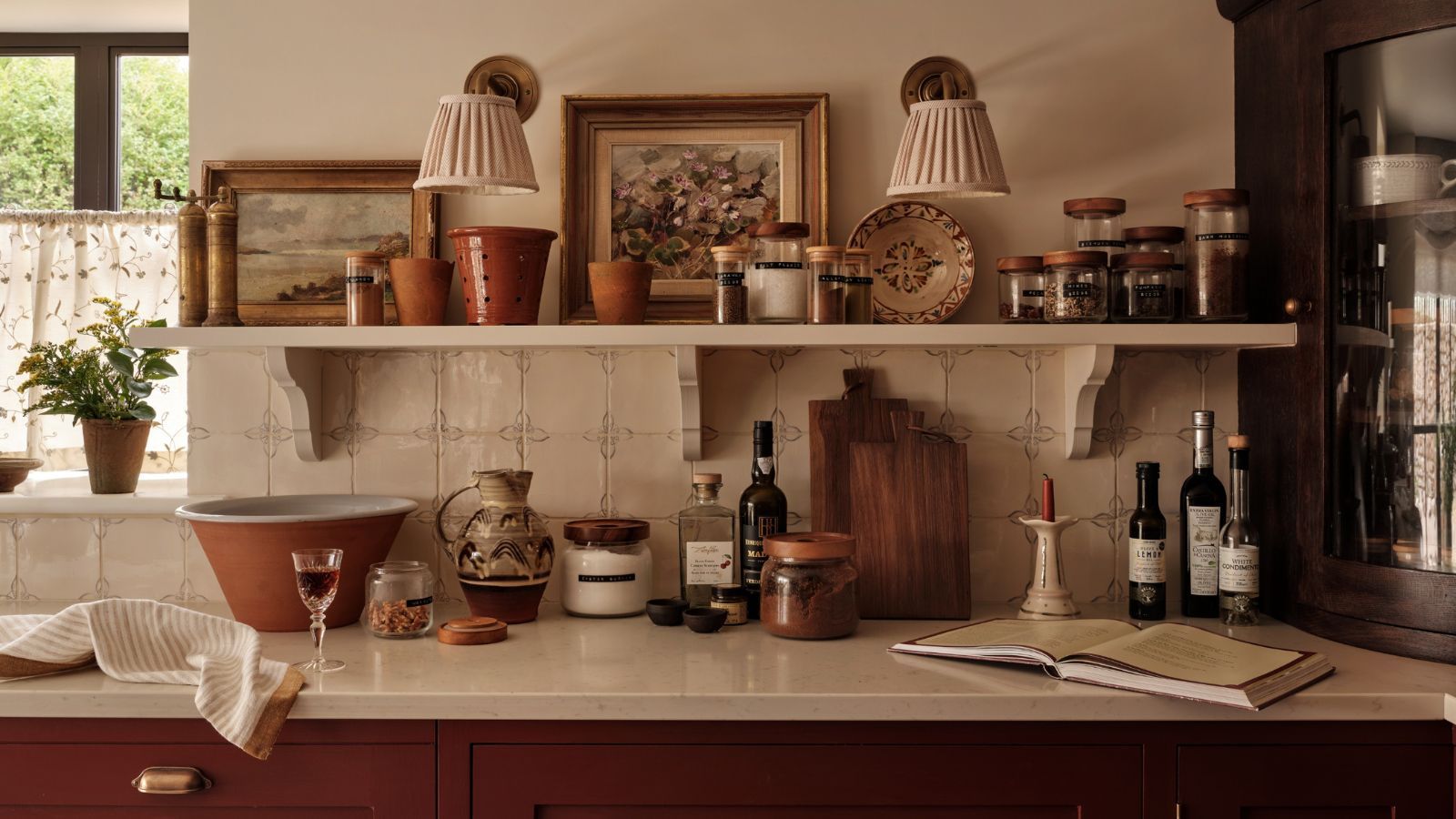 A kitchen with red cabinets, white worktops and white tile backsplash. Close up of the counter and a wall-mounted shelf covered in cozy kitchen clutter.