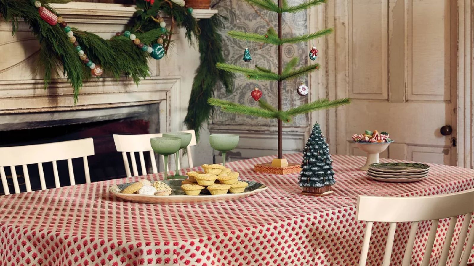 Red and white leaf tablecloth with green frosted coupe glasses and a Christmas tree candle
