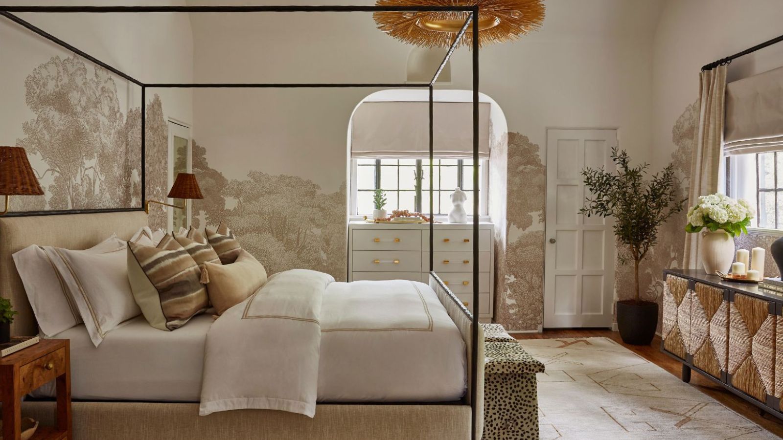 Neutral bedroom with four poster black metal bed, botanical neutral wallpaper, cream carpet, textured sideboard