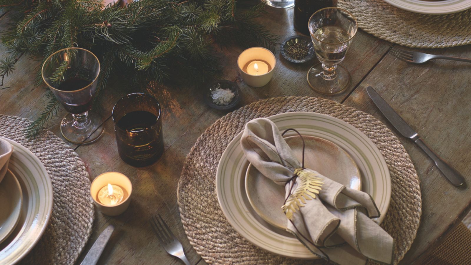 Wood dining table with rattan placemats, wreath centerpiece, and gold leaf-shape napkin rings