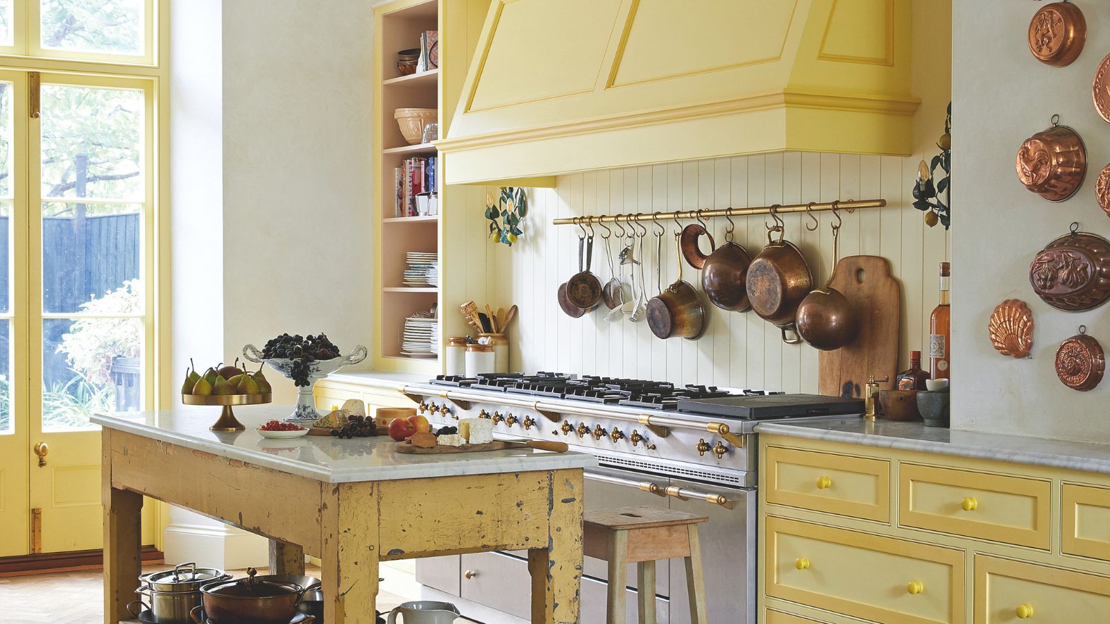 Yellow kitchen styled with vintage pots, accessories and copper jelly moulds hanging on the wall
