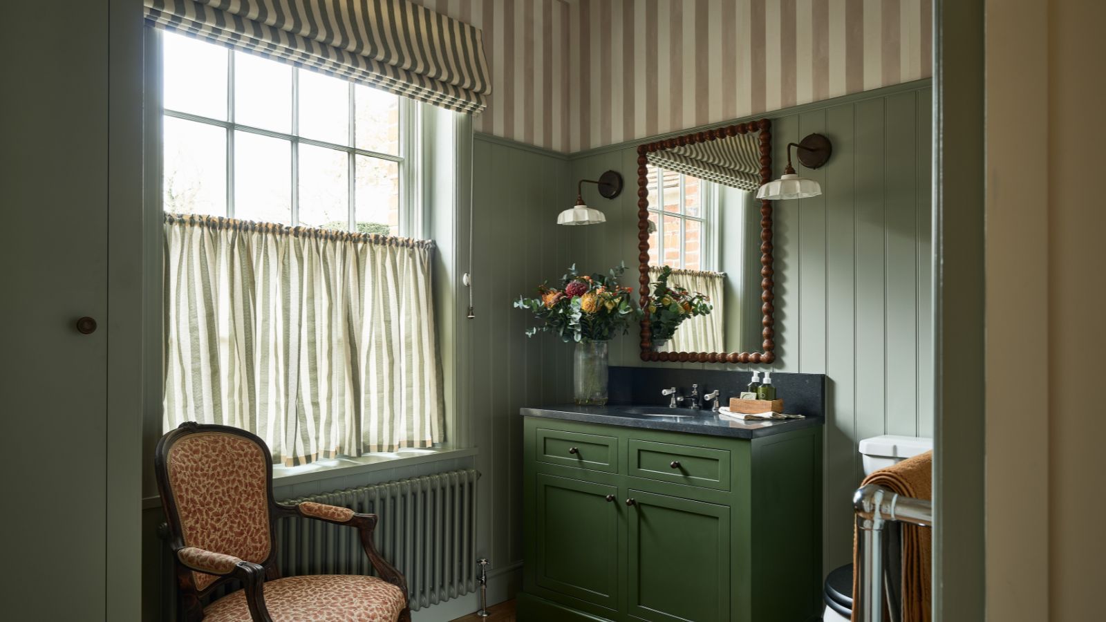 A green paneled powder room with striped wallpaper ceiling