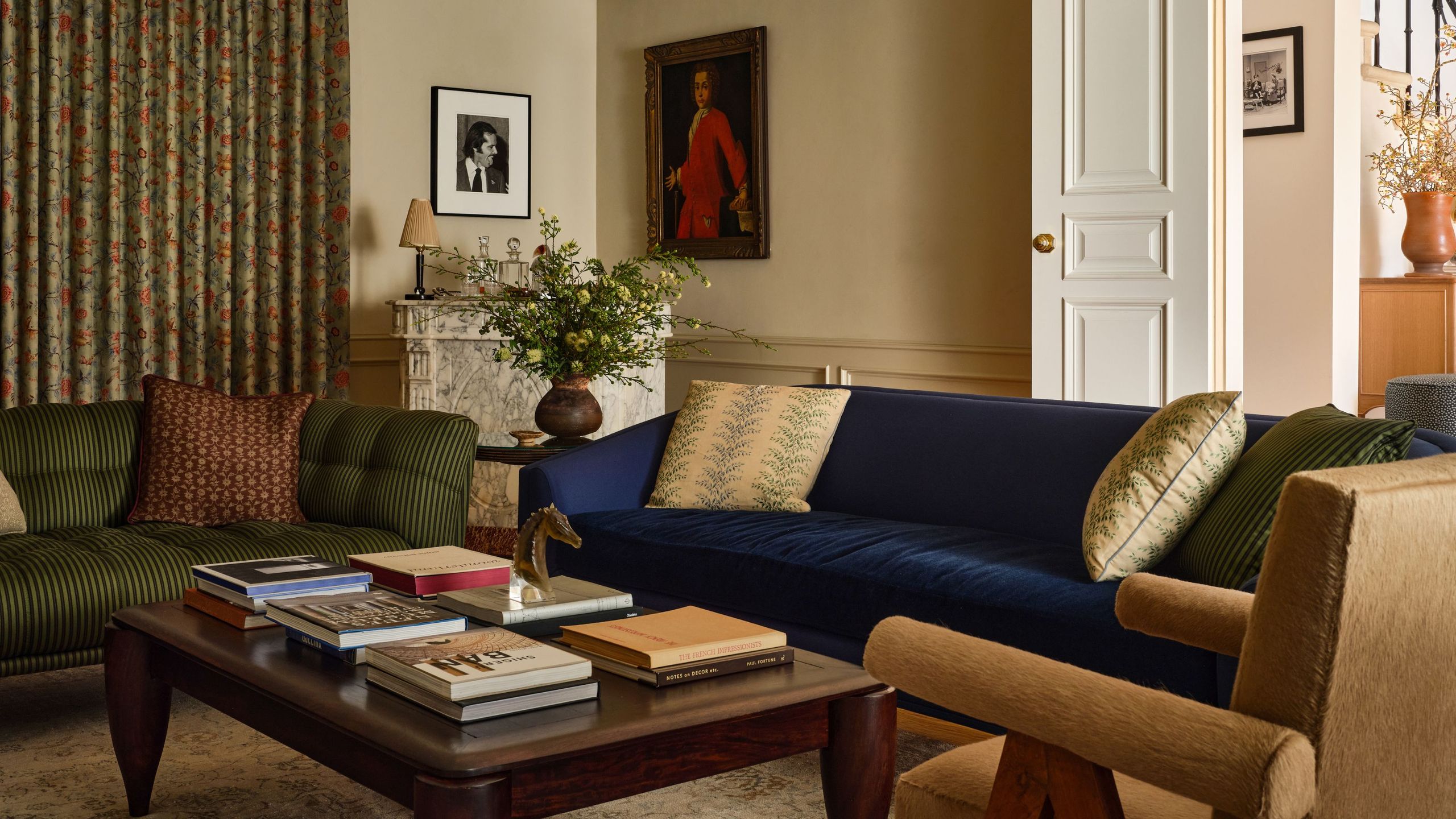 Cozy living room with a navy velvet sofa, a striped olive green sofa, an orange upholstered armchair, and a dark wood coffee table in front of a marble fireplace