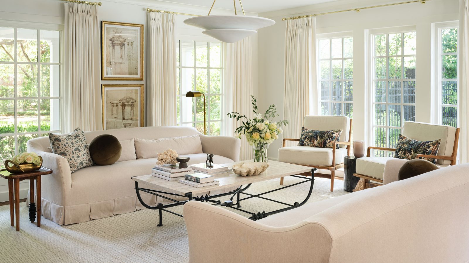 warm minimalist living room with all neutral decor, a wrought iron coffee table, arm chairs with foliage printed cushions and a skirted couch