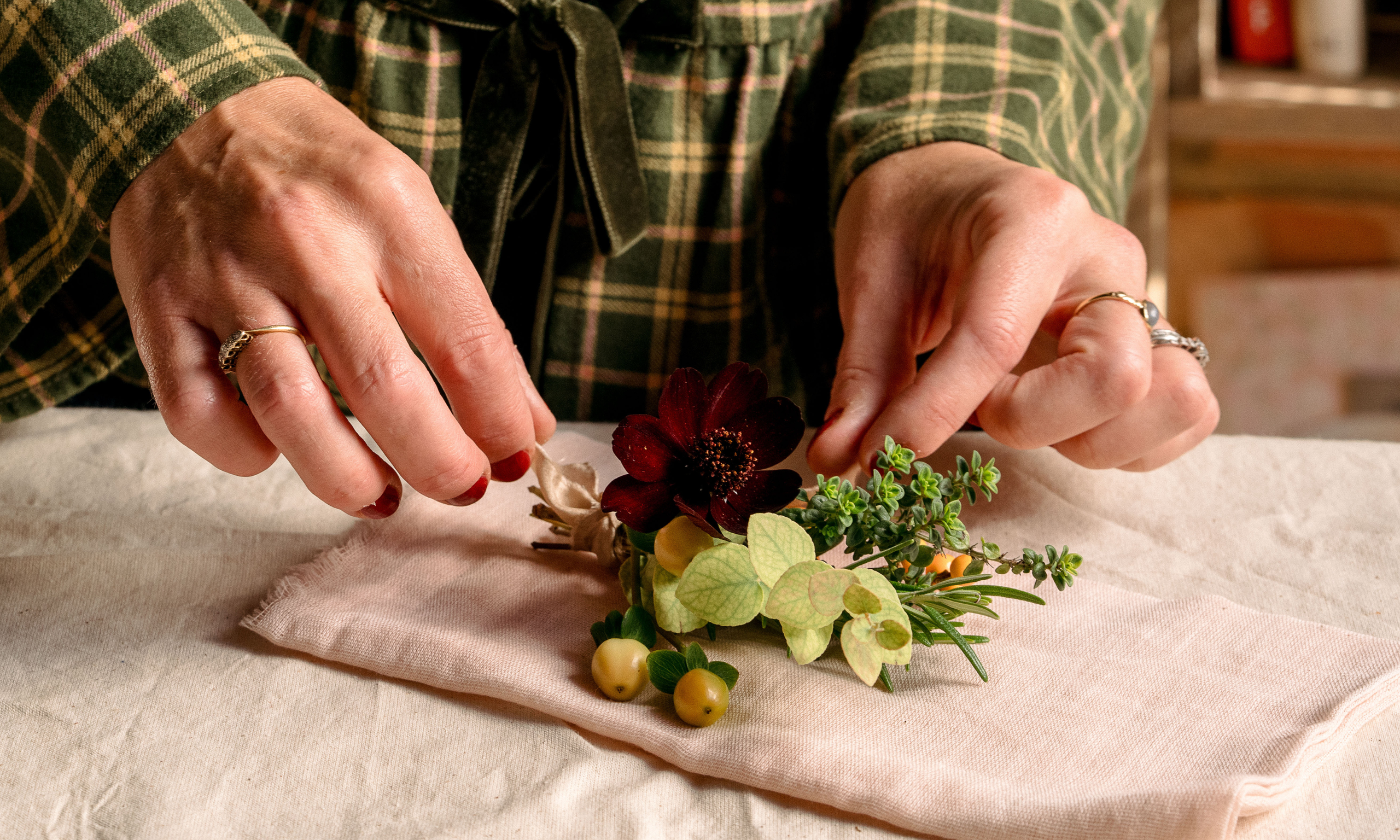 Hands arranging flowers and foliage on a pink cotton napkin