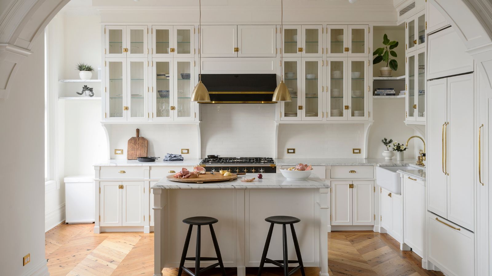 Fitted white country kitchen through period archway with kitchen island and brass fittings on parquet floor