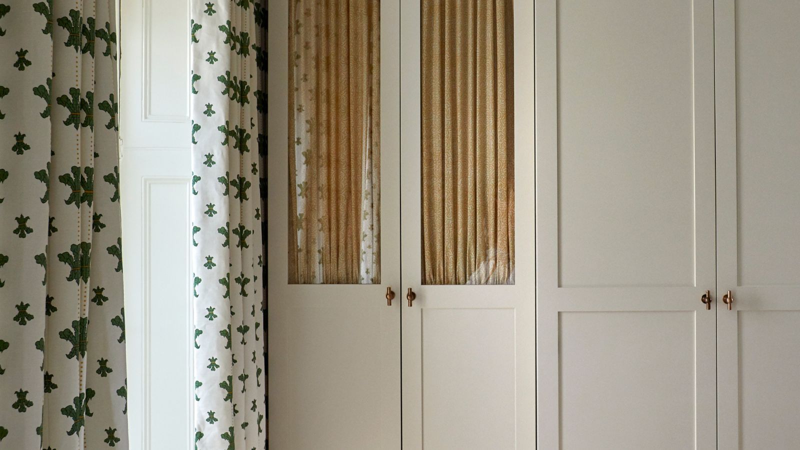 neutral wardrobes with glass front closet door with a cabinet curtain behind and brass hardware