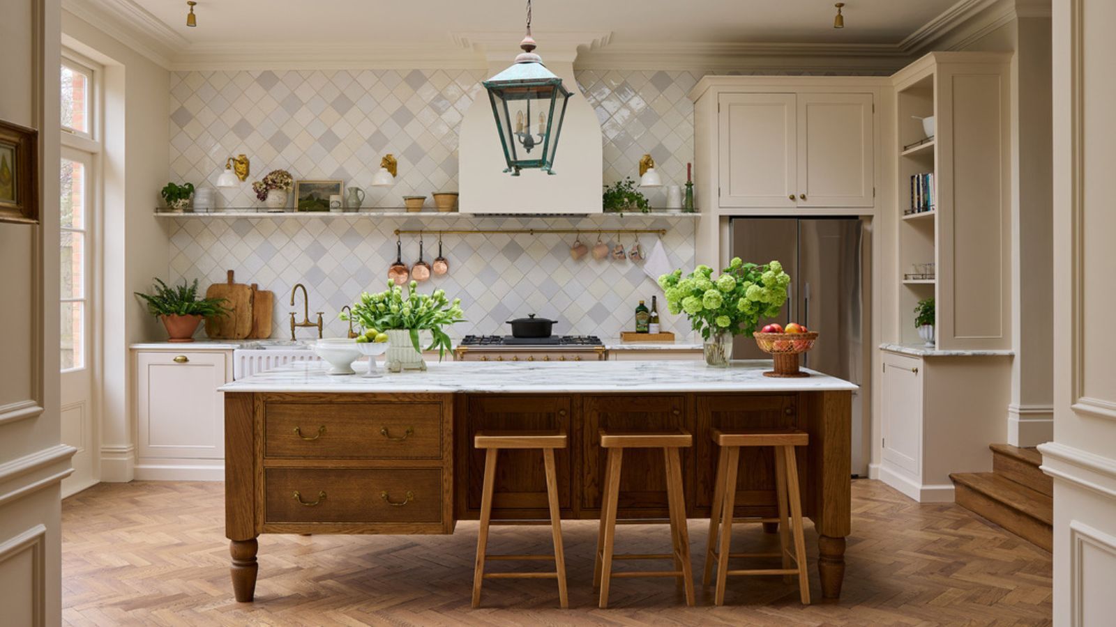 A warm neutral kitchen with cream cabinets, a wooden island, marble countertops, and a tiled backsplash