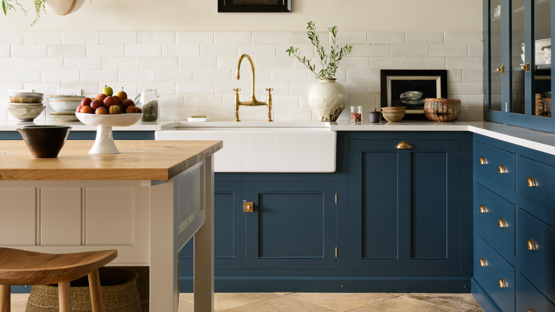 White kitchen with dark blue deVOL cabinets, wooden floors and wooden island with white sides and basket storage underneath