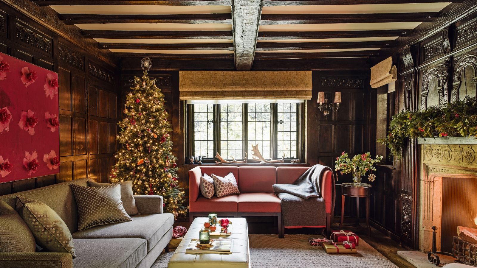 A cozy living room with two sofas, with exposed ceiling beams, a tall decorated Christmas tree and fireplace with a lit fire.