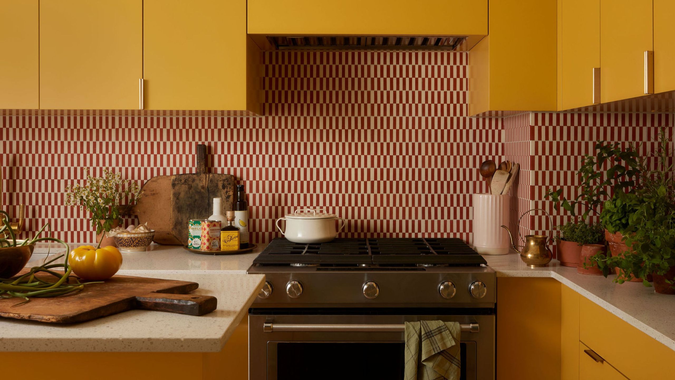 Close-up of a sunny yellow kitchen counter with a stove, a toaster, potted herbs, and an open cabinet revealing dishes and bottles