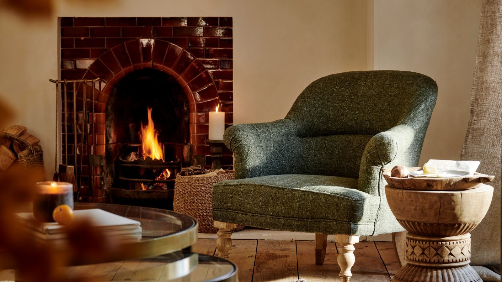 An upholstered green armchair beside a brick fireplace in a cream living room.