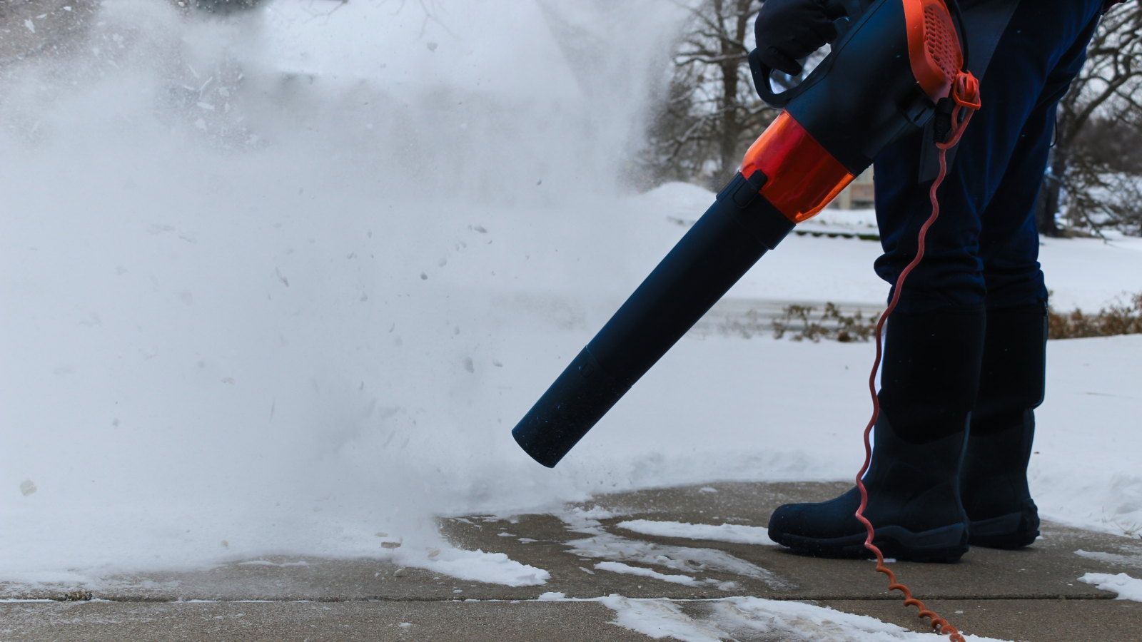 A person is using a corded leaf blower to blow snow from their driveway