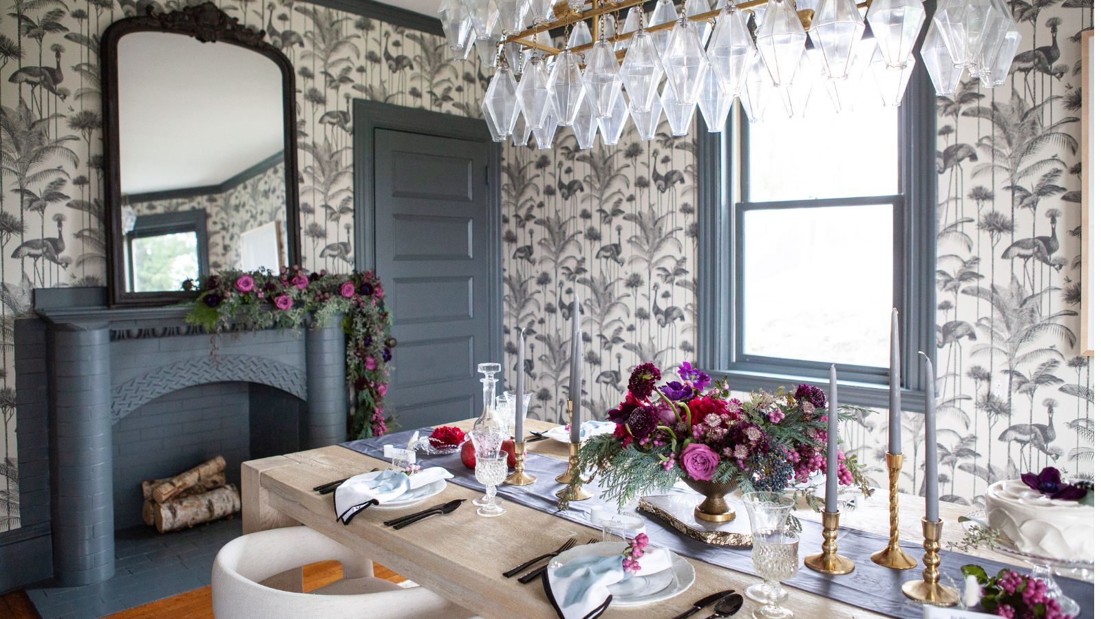 Dining room with intricate wallpaper, mantel place and glass ceiling light feature, as well as painted wooden doors, window frames, mantel surround in chalky mid-blue hue