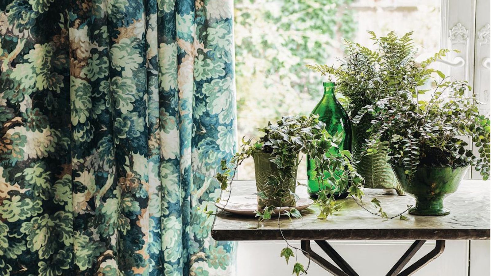 Range of houseplants on a table next to a blue and green patterned curtain