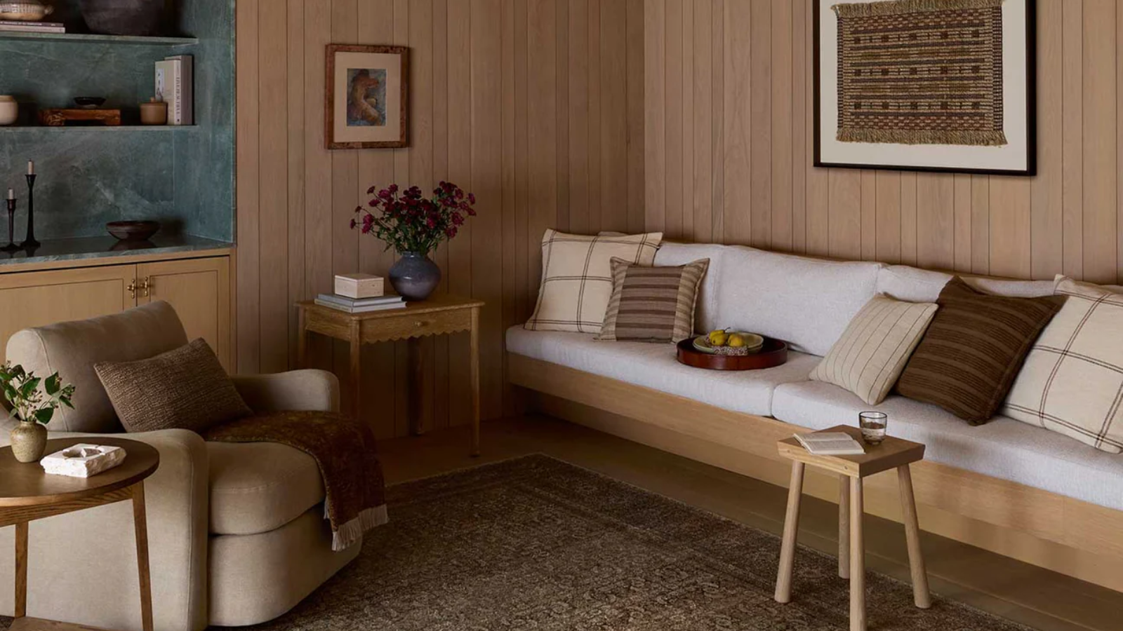 a warm living room with a built-in couch with pillows on top, a brown swivel chair, a stool, and a side table with flowers on it