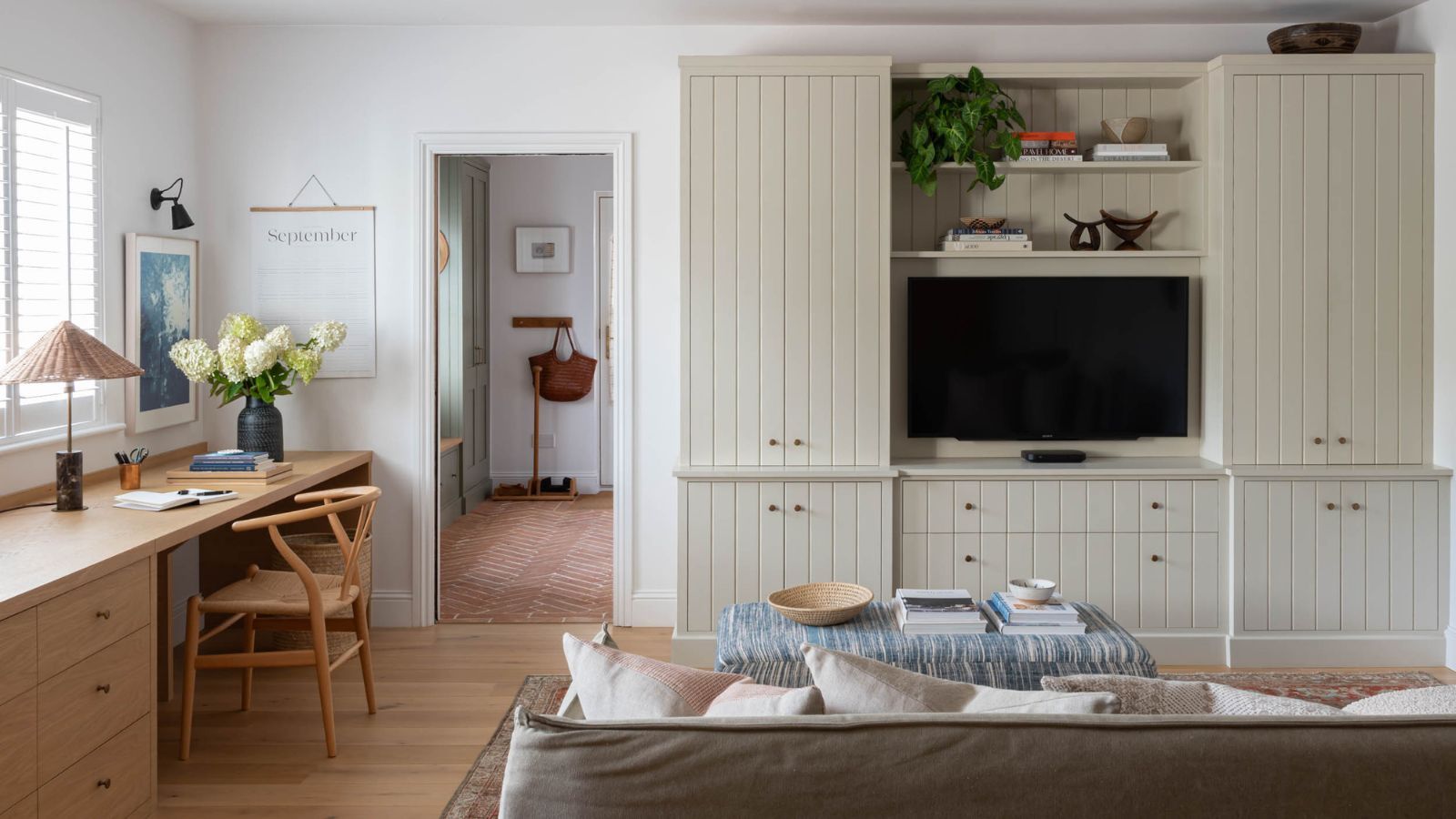 A living room with a long built-in desk along one wall, and a built in media unit on the adjacent.