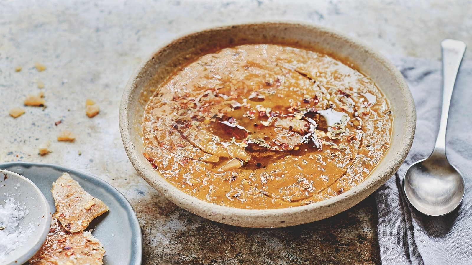 Pumpkin and apple soup in a bowl with a plate of crackers