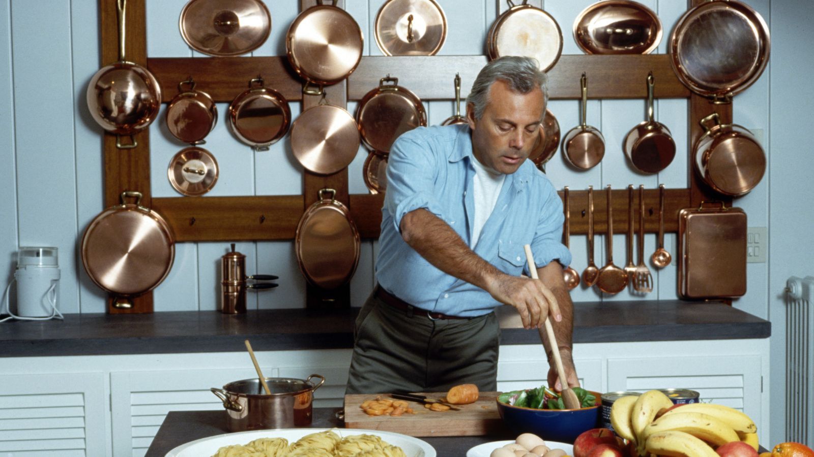 Giorgio Armani in his kitchen with copper cookware hanging on wall