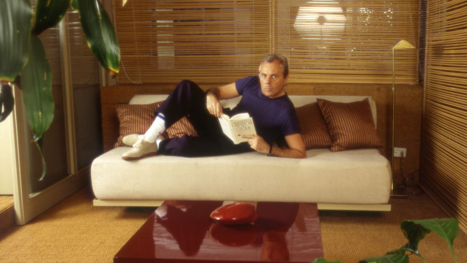 Giorgio Armani in his living room with a red lacquer coffee table, bamboo blinds and a cream sofa bed