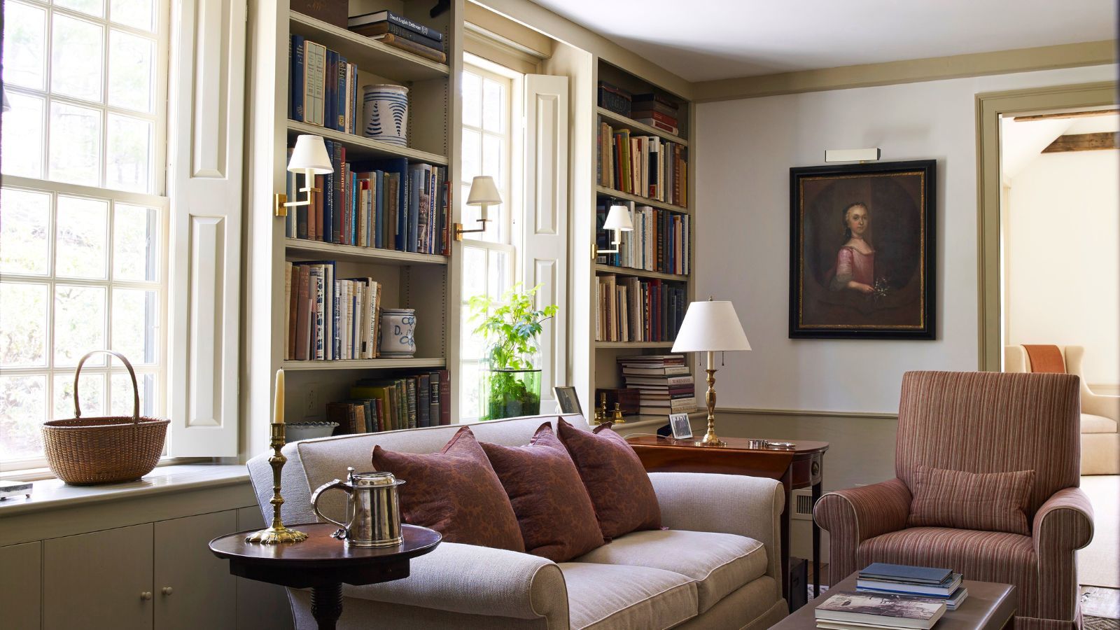 A cozy living room with build in book shelves between windows. A cream sofa in front beside a brown upholstered arm chair.