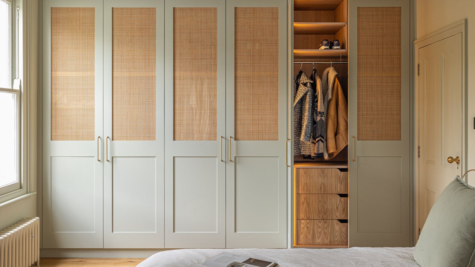 A blue built-in closet with rattan window panels. One door open showing a hanging rail and drawers beneath.