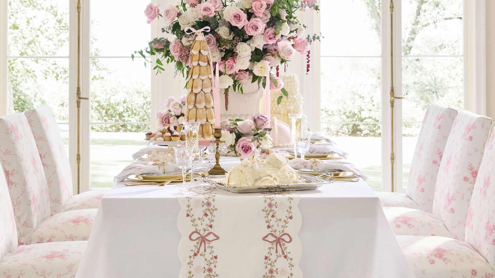White table with pink floral dining chairs, a pink bow table runner, and gold chargers