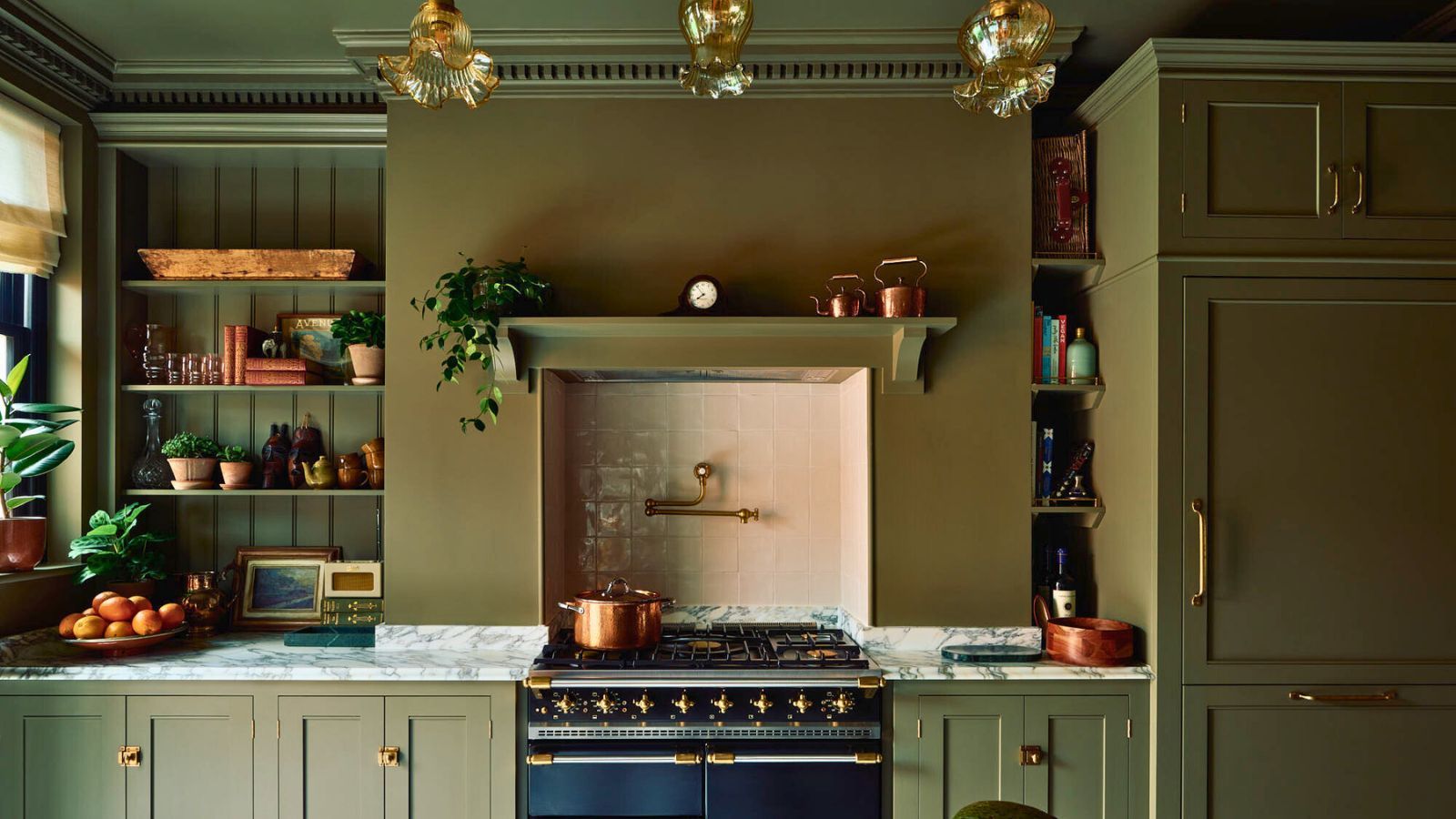 Dark green kitchen with Range cooker and shelving, with crown molding on the ceiling, pearly stovetop splashback and brass touches