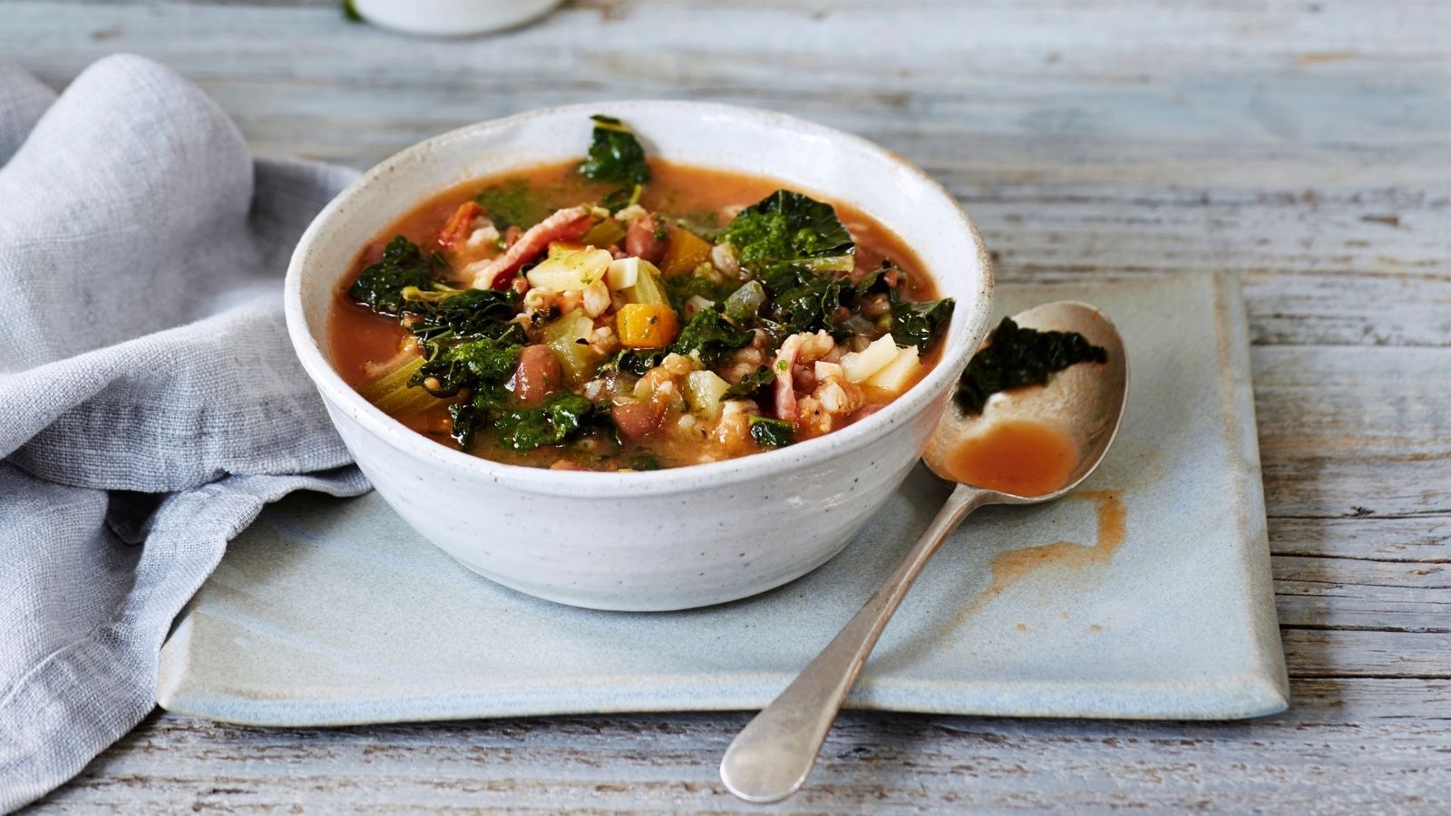 Bowl of vegetable soup on a gray table with napkin and spoon