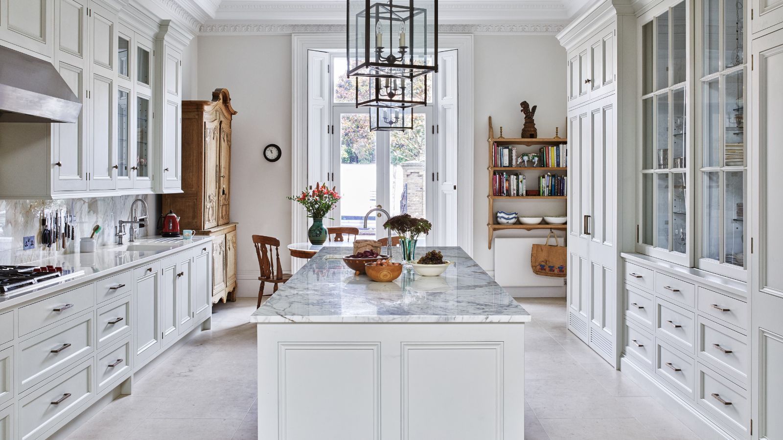 A white kitchen with marble island, white and glass cabinets, and wooden shelves and dresser.