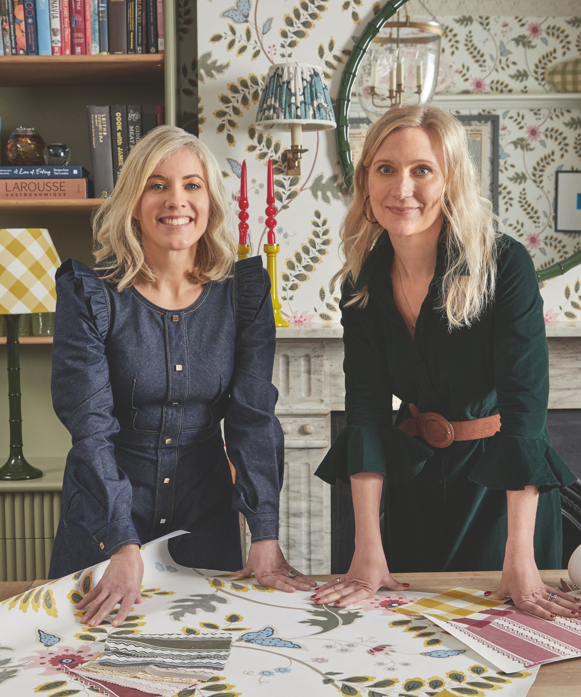 Zwei Frauen stehen an einen Tisch gelehnt, auf dem Tapetenmuster verstreut liegen