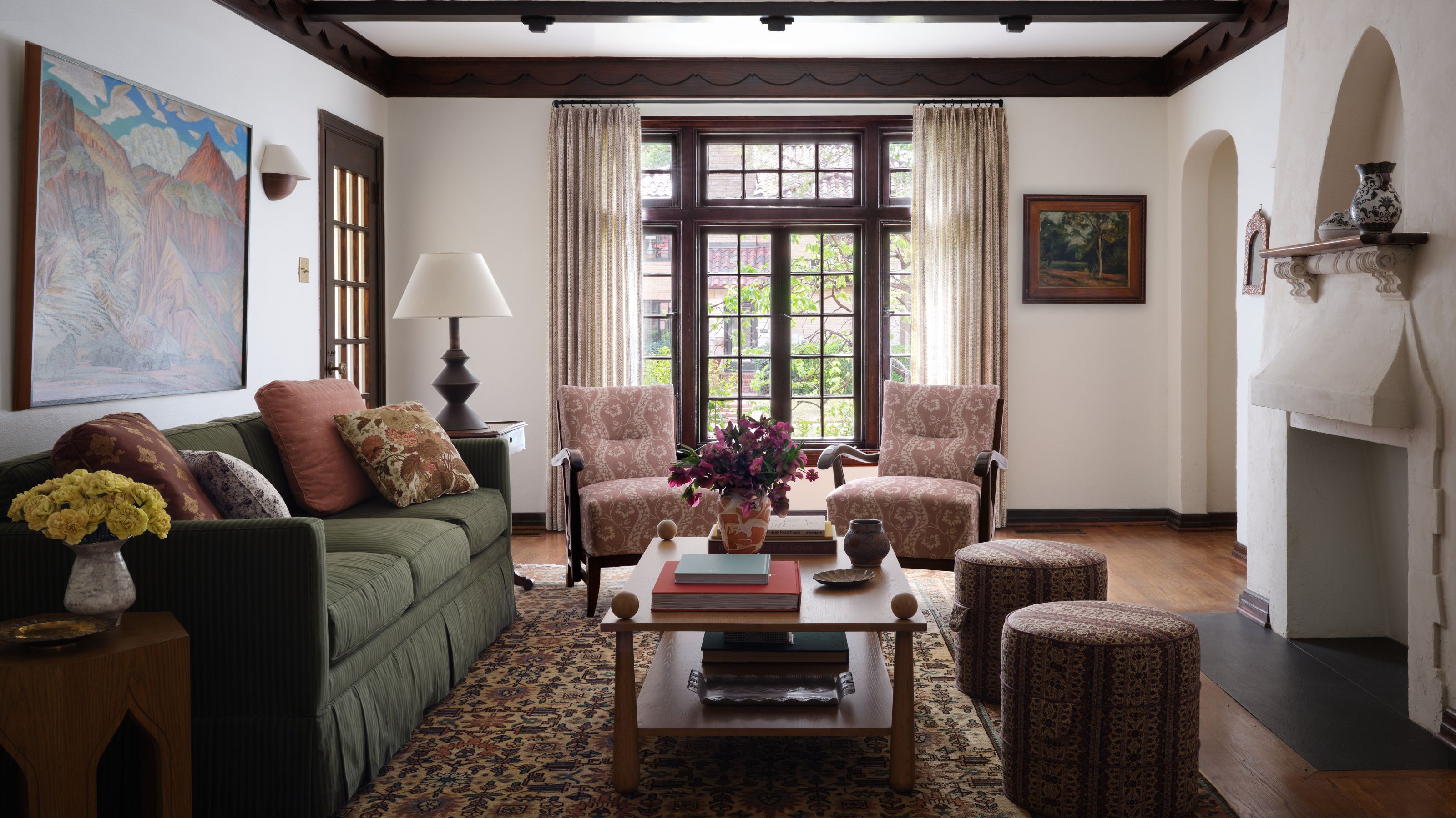 Eine weite Ansicht eines Wohnraums mit einem grünen Sofa, einem Landschaftsgemälde und einem verzierten Kamin aus weißem Gips mit einer Nische mit Spitzbogen