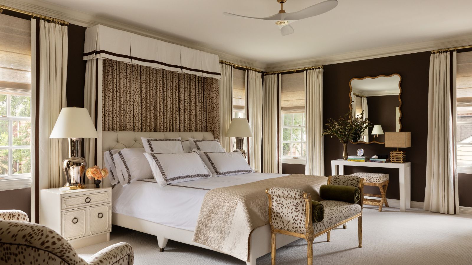 A bedroom with dark brown walls, a large bed with a tall fabric headboard, cream carpet, and cream decor.