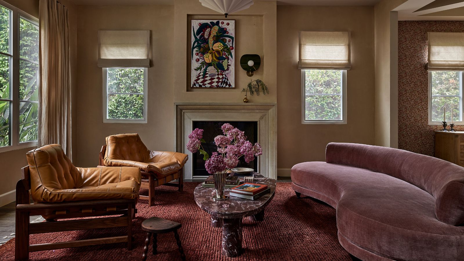 Ein modernes Wohnzimmer mit neutralen Wänden, einem Kamin, einem pflaumenfarbenen Teppich und einem malvenfarbenen, geschwungenen Sofa. 