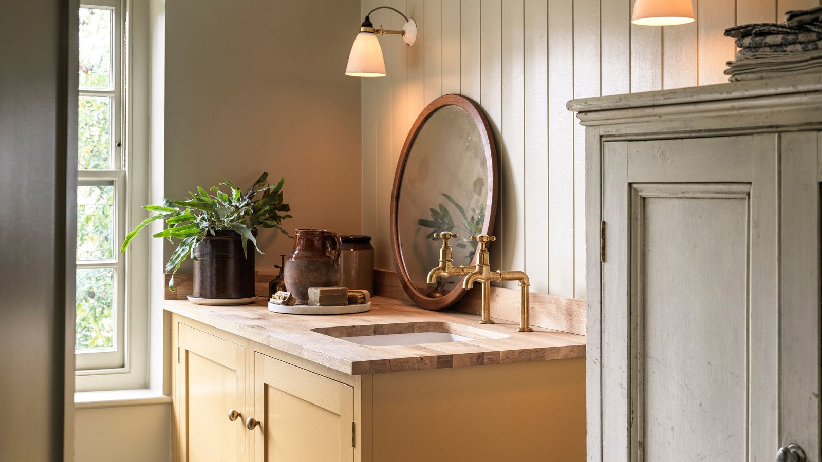 Ein gelb lackierter Waschtisch mit einer Holzplatte. Zwei Messinghähne und ein eingelassenes Waschbecken