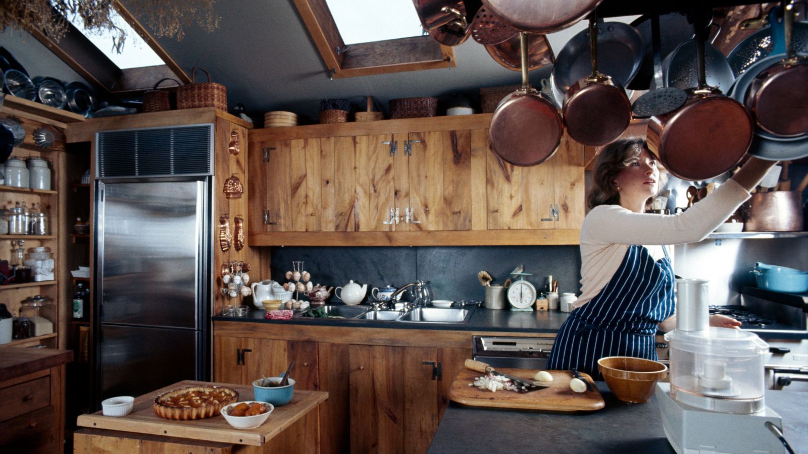 Martha Stewart in ihrer Küche mit Holzschränken, Kupferkochgeschirr und offenen Regalen voller Gläser und Kupfergefäße