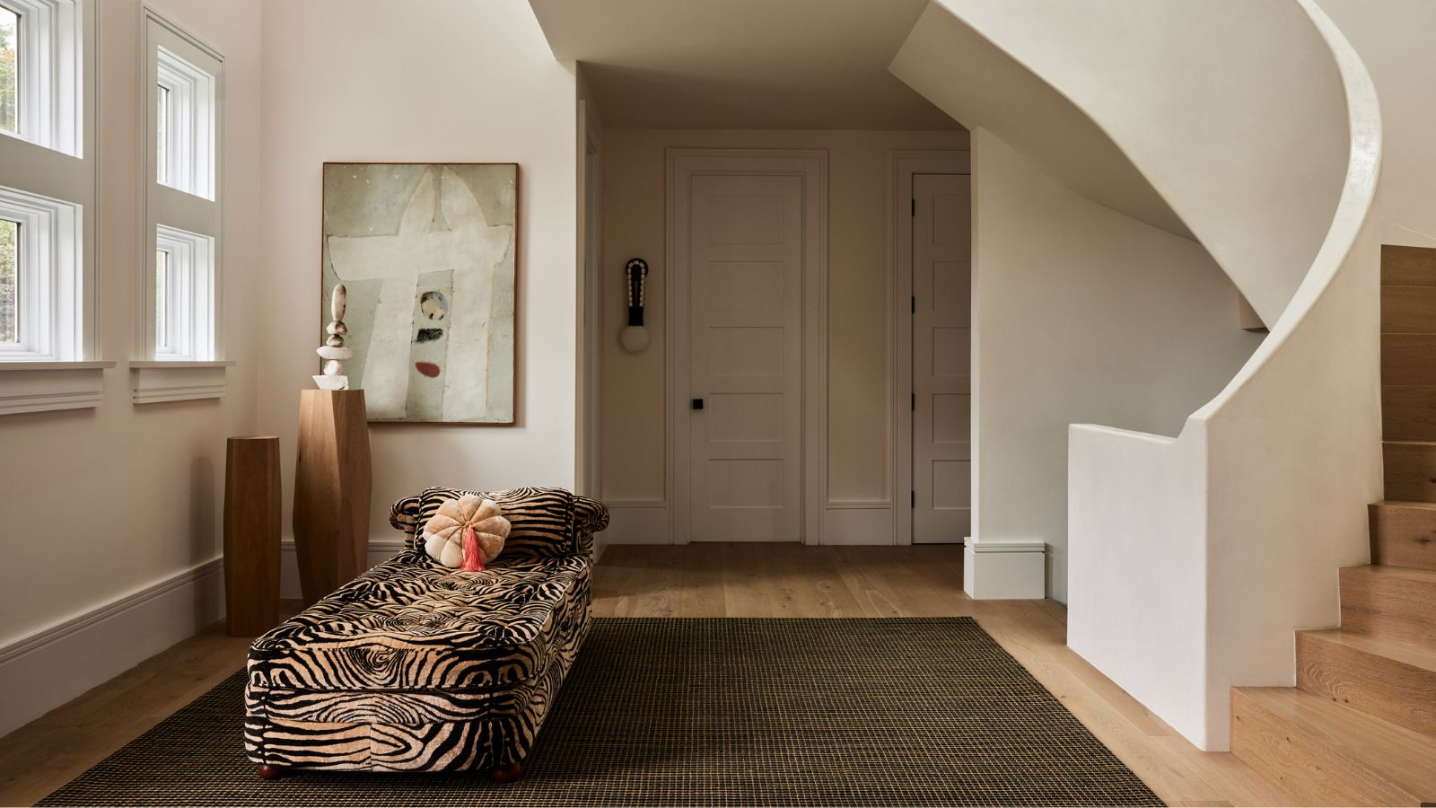 Eingangsbereich mit Wendeltreppe, großem olivgrünen Teppich auf Holzboden, Tagesbett mit Tigermuster und samtrosa Kissen und modernem abstrakten Gemälde im Hintergrund