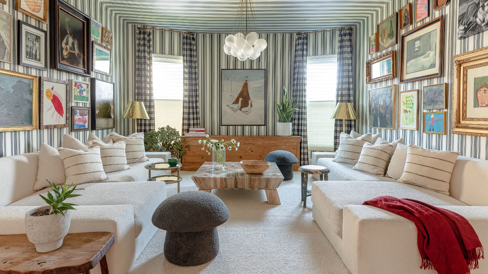 Maximalistisches Wohnzimmermuster mit gestreiften Tapeten an Wänden und Decke, Gingham-Vorhängen, zwei Vintage-Galeriewänden auf gegenüberliegenden Seiten und zwei passenden weißen Ecksofas mit einem Pilzhocker