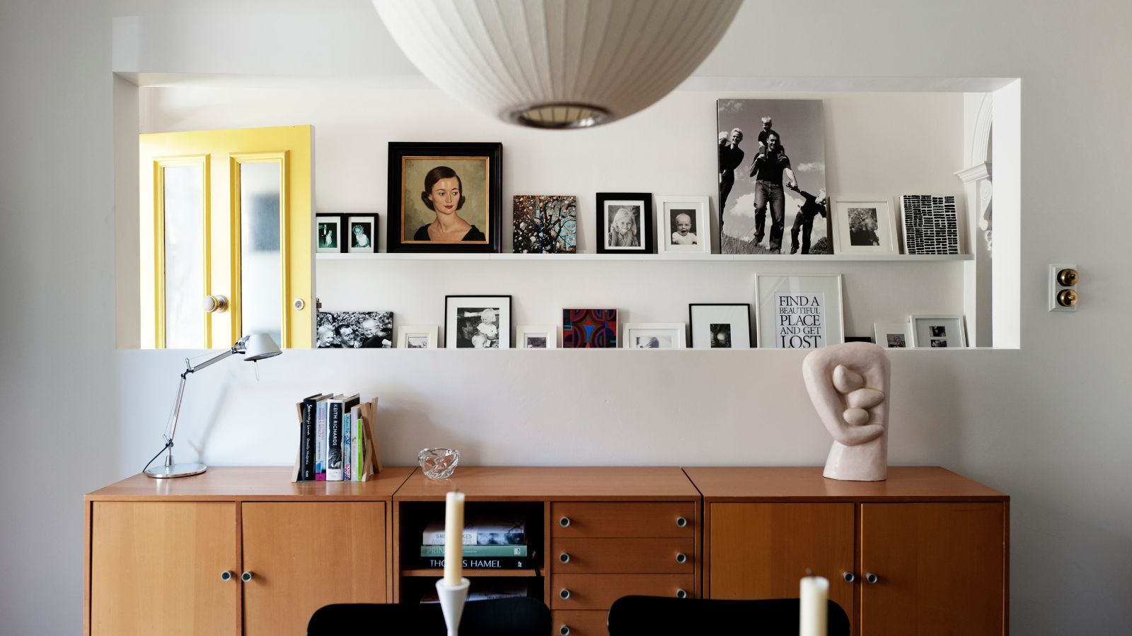 Entryway with a yellow front door, picture ledges along the wall with framed prints and photos, midcentury console, and a lantern pendant light