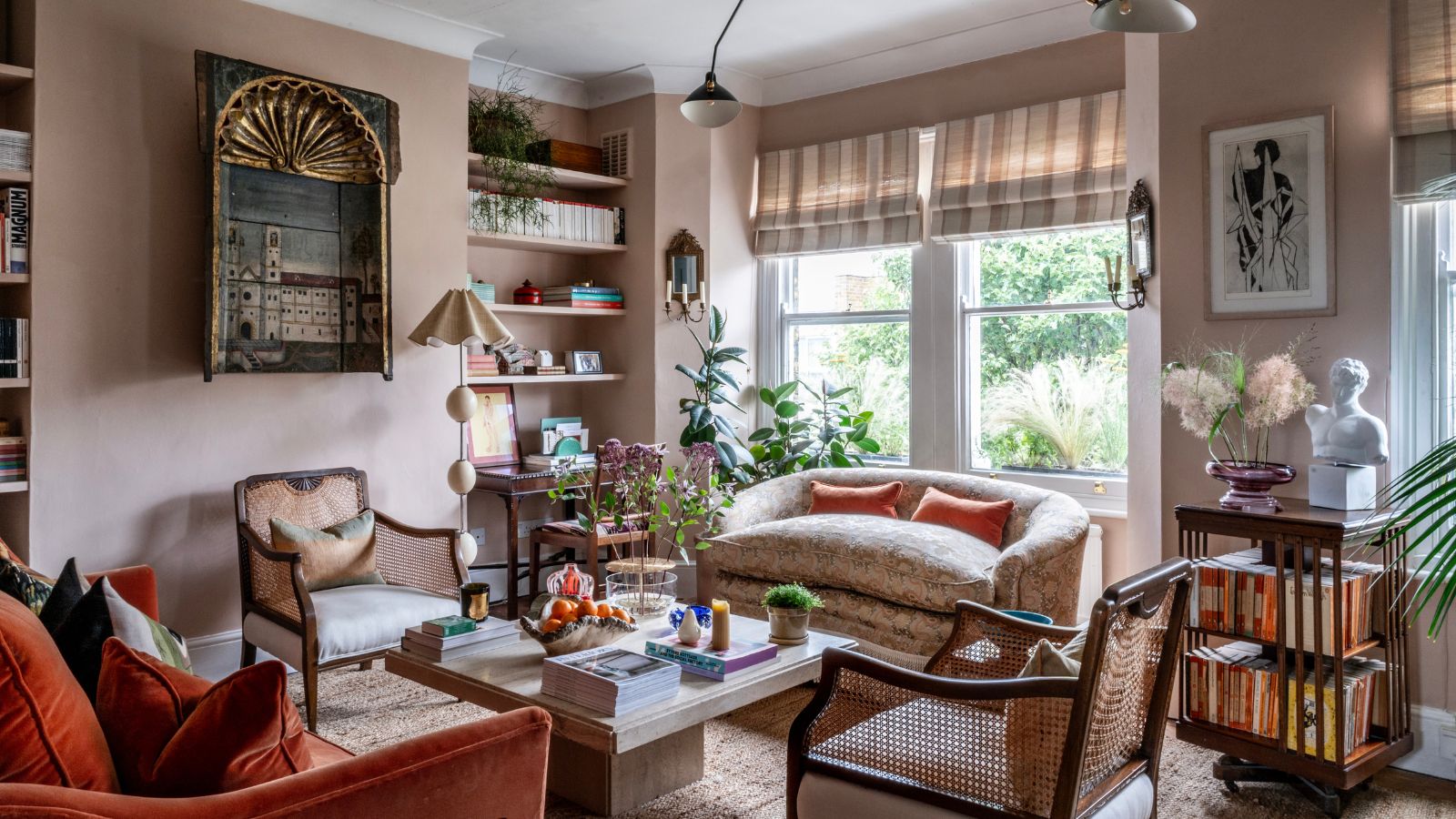 Übergangswohnzimmer mit blassrosa Wänden, orangefarbenem Samtsofa, Hängelampe aus der Mitte des Jahrhunderts, antiker Kunst, Marmor-Couchtisch mit Dekor 