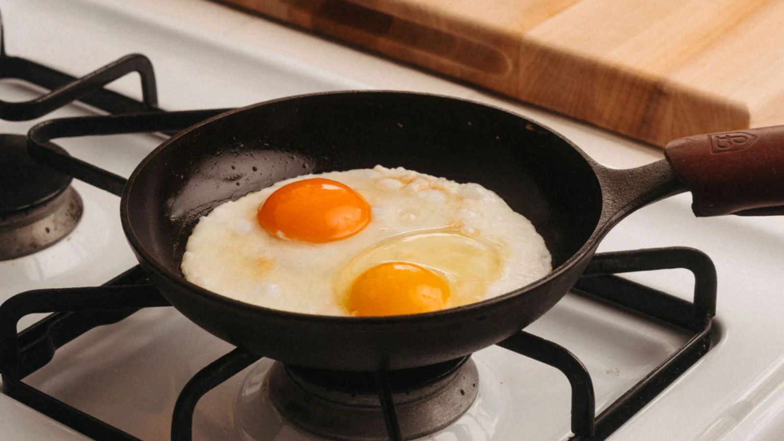 Field Company Cast Iron Skillet with two frying eggs inside on a gas stove.