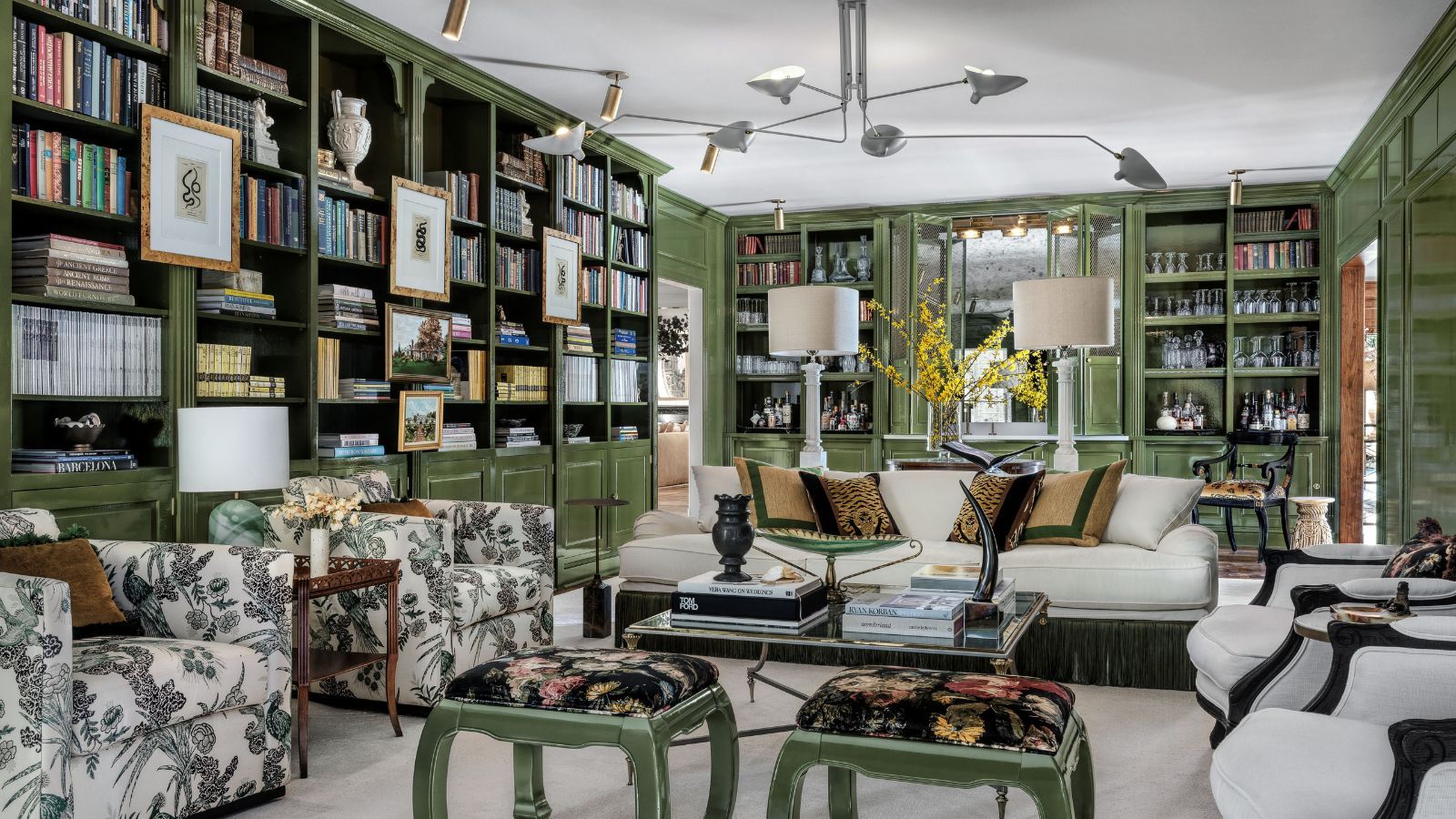 Living room with green painted bookshelves, cream sofa and armchairs, midcentury pendant light, green stools