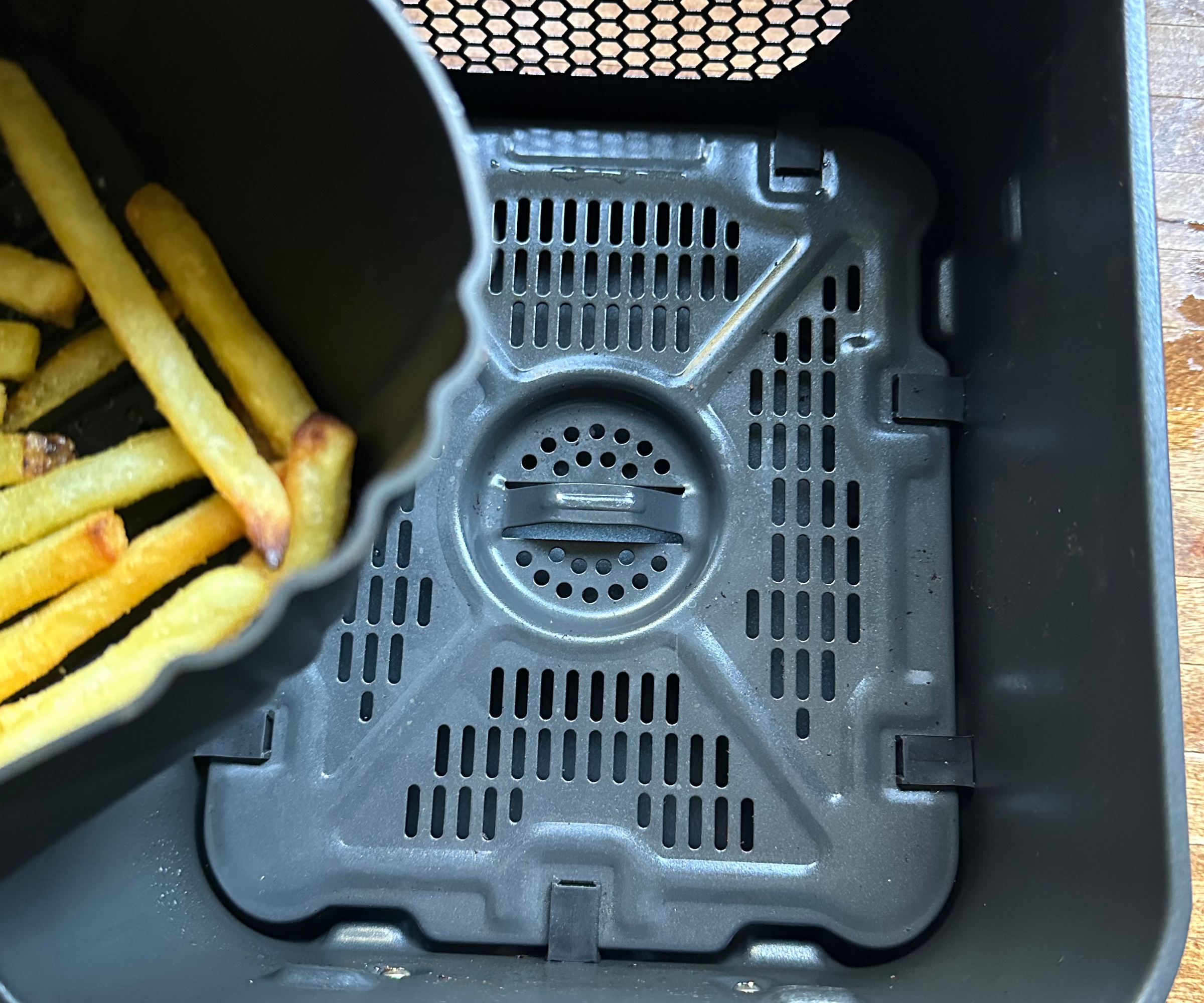 Ein sauberer, leerer Heißluftfritteuse-Korb, an dessen Seite die Ecke einer mit Pommes Frites gefüllten Silikon-Heißluftfritteuse-Korbauskleidung sichtbar ist.