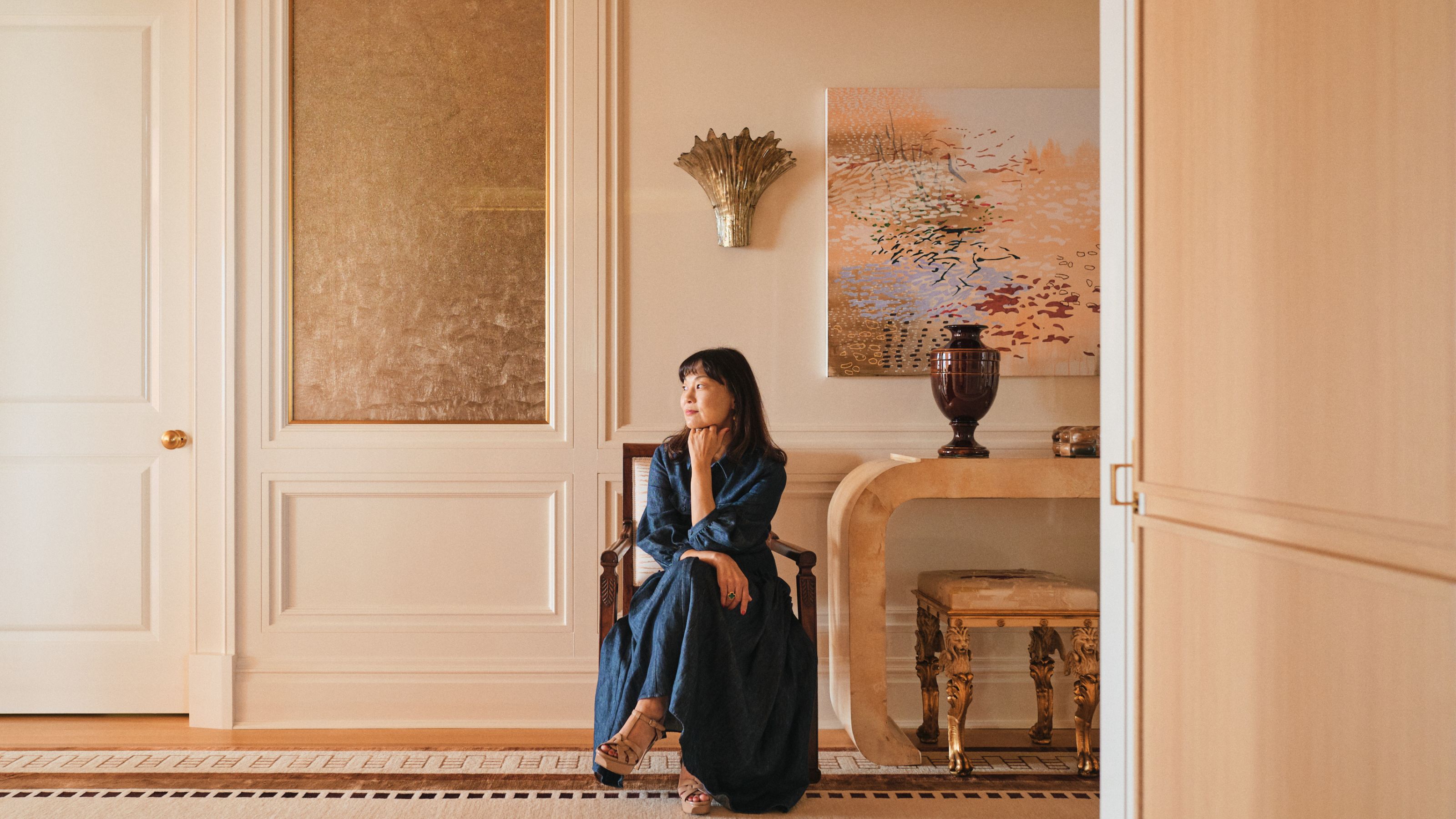 Der junge Huh sitzt auf einem Stuhl in einem cremefarbenen Eingangsbereich und blickt verträumt von der Kamera weg und zur Seite