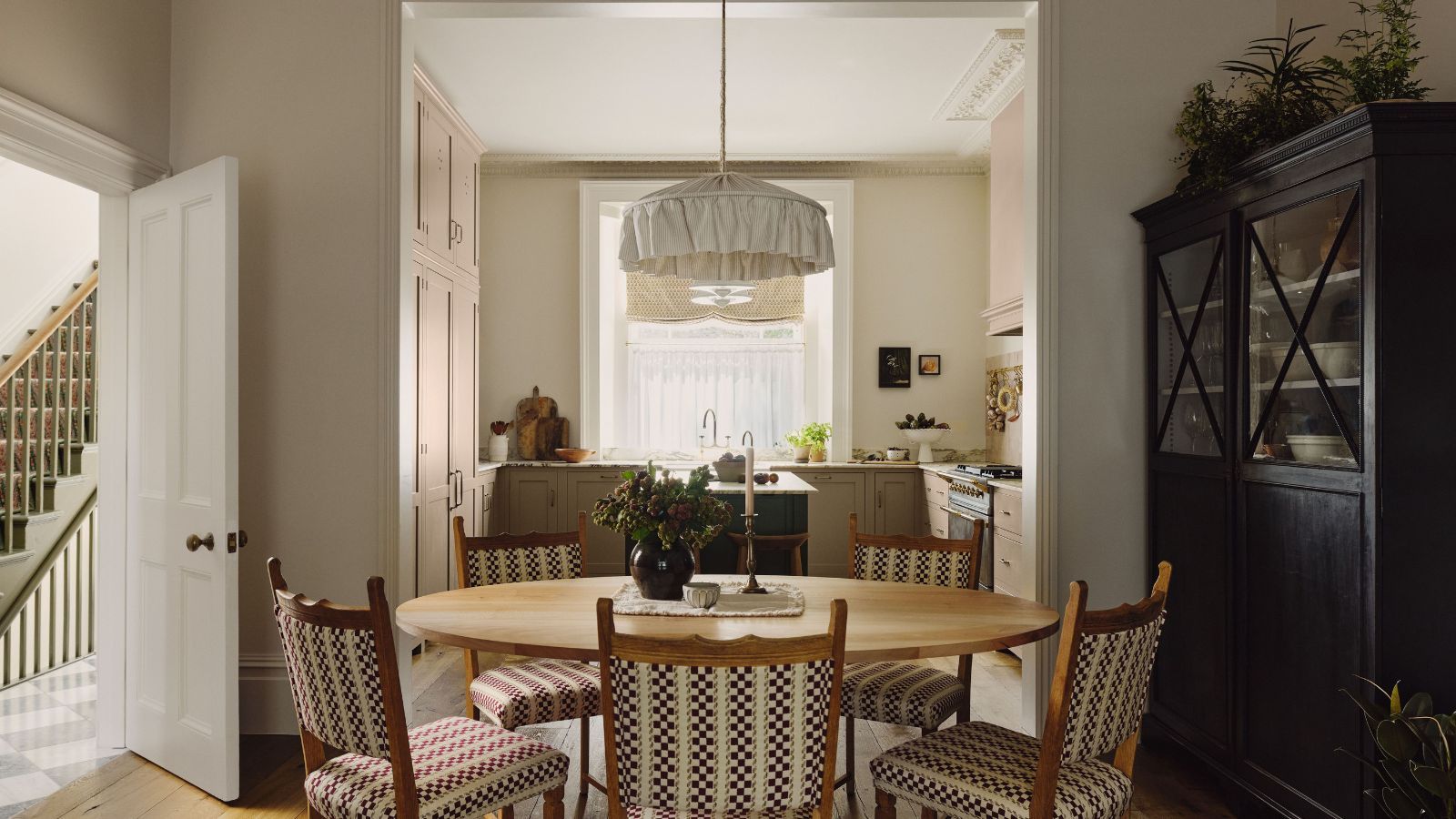 Breakfast table with bistro chairs, low pleated pendant lights, black armoire with tableware looking into the kitchen