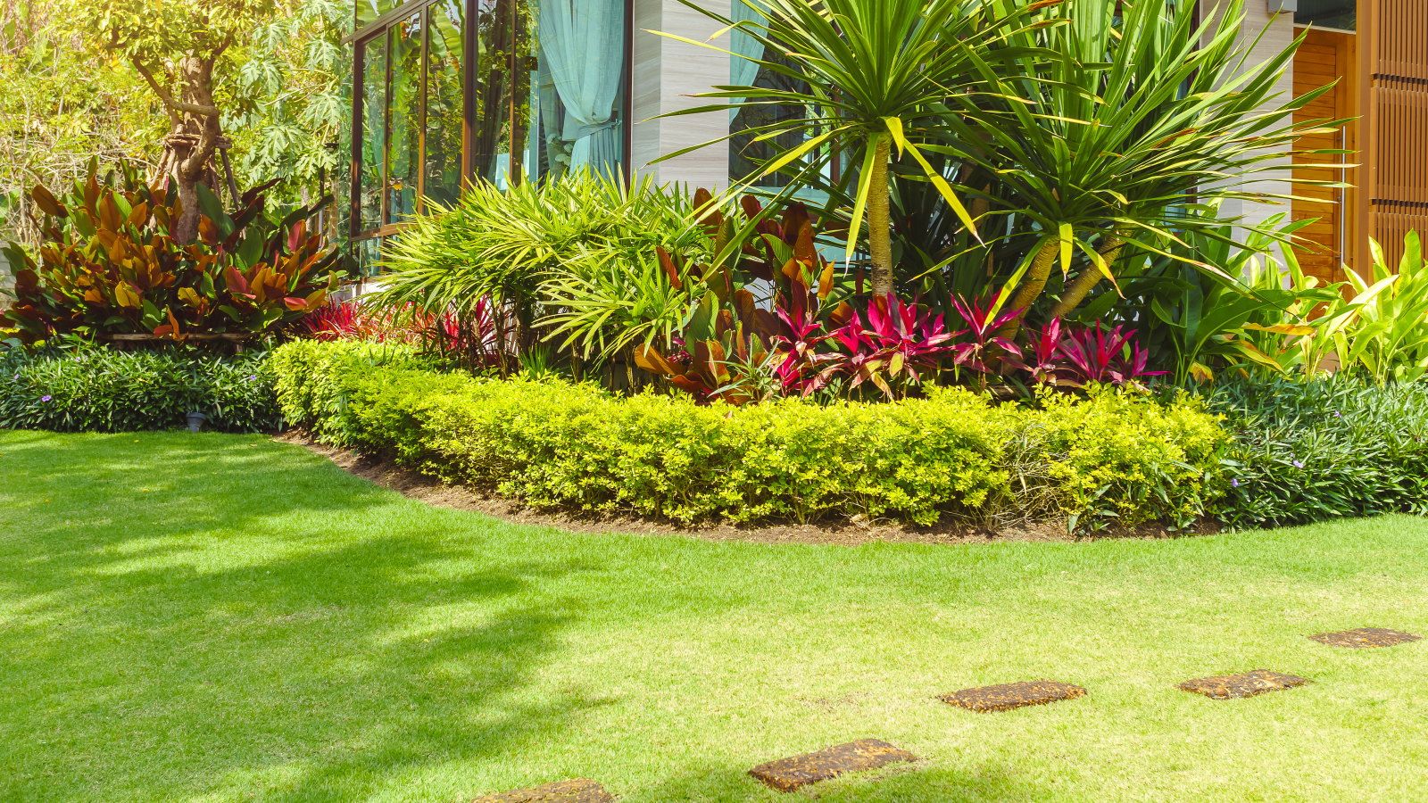 A house with a green, lush front lawn and tropical planting
